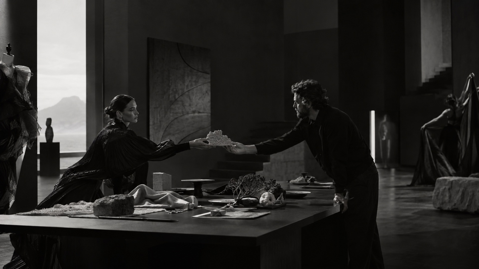 Two makers exchanging a sculptural material sample in a dark gallery workspace